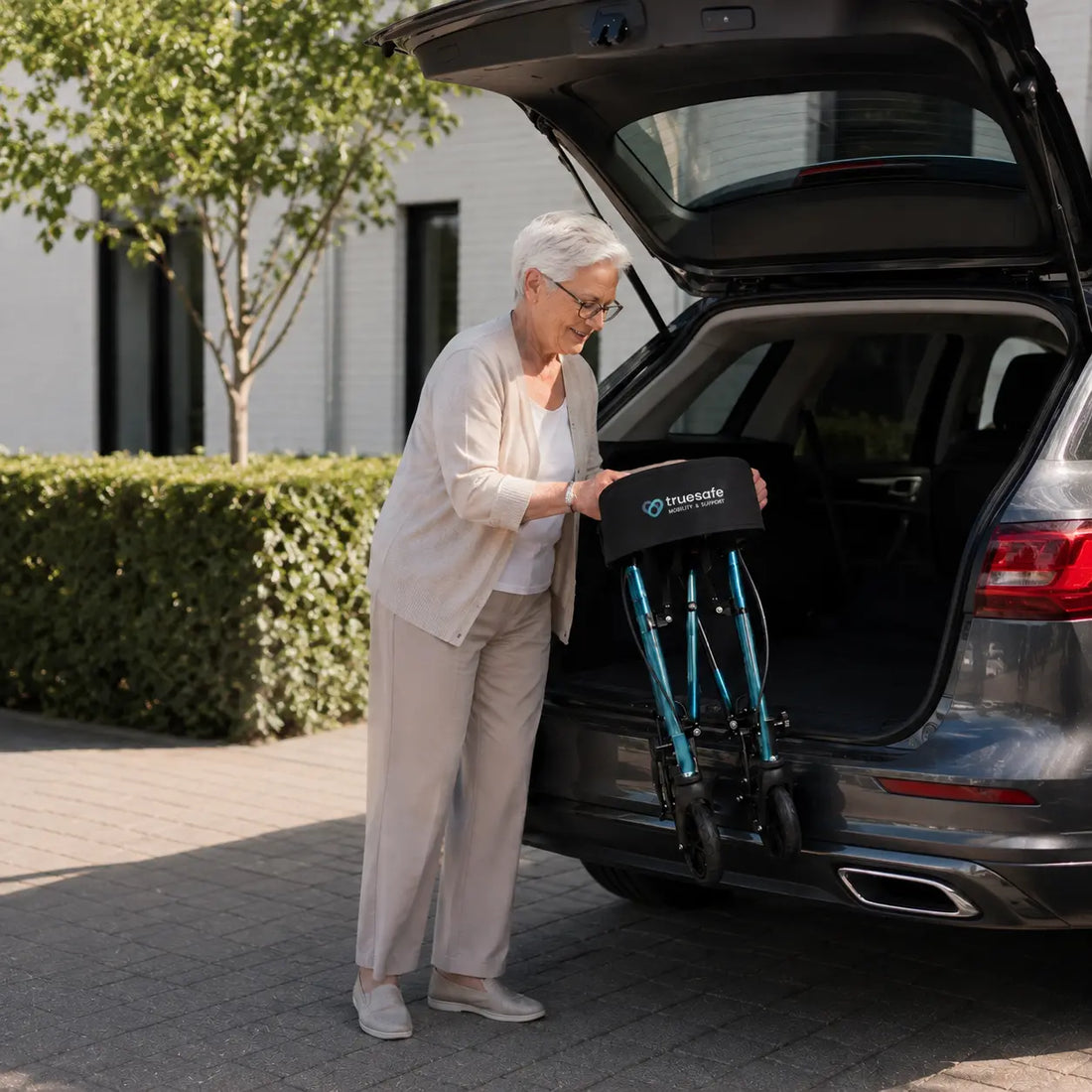 Oudere vrouw plaatst de opvouwbare TrueSafe rollator eenvoudig in de kofferbak van een auto dankzij het lichte en compacte ontwerp.